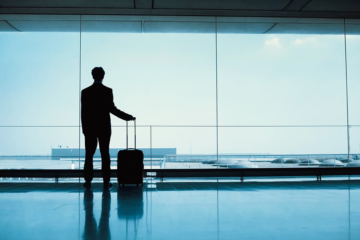 Profissional com mala de viagem junto a uma janela de aeroporto.
